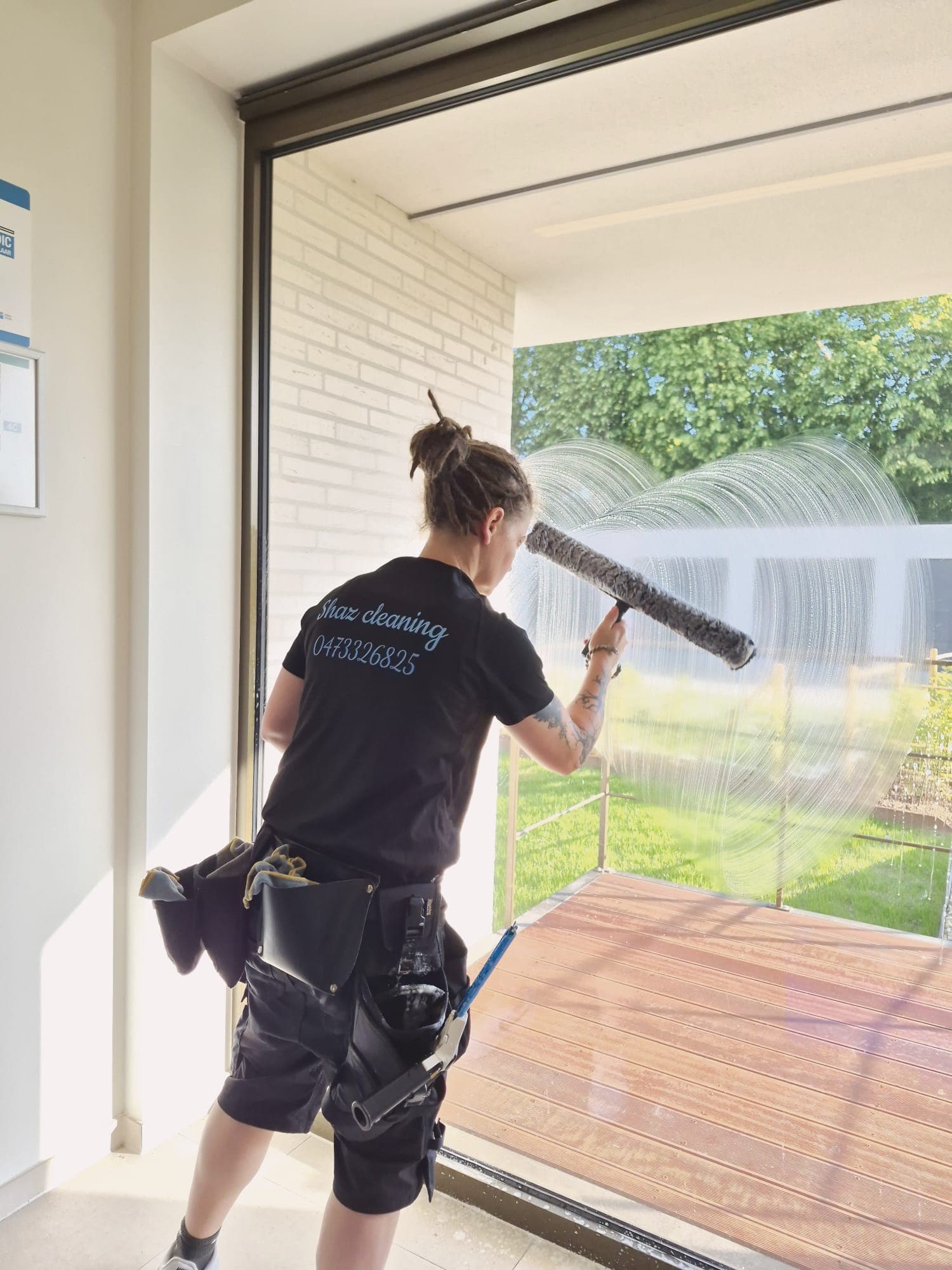 Medewerker van Shaz Cleaning poetst een groot raam met bedrijfsshirt