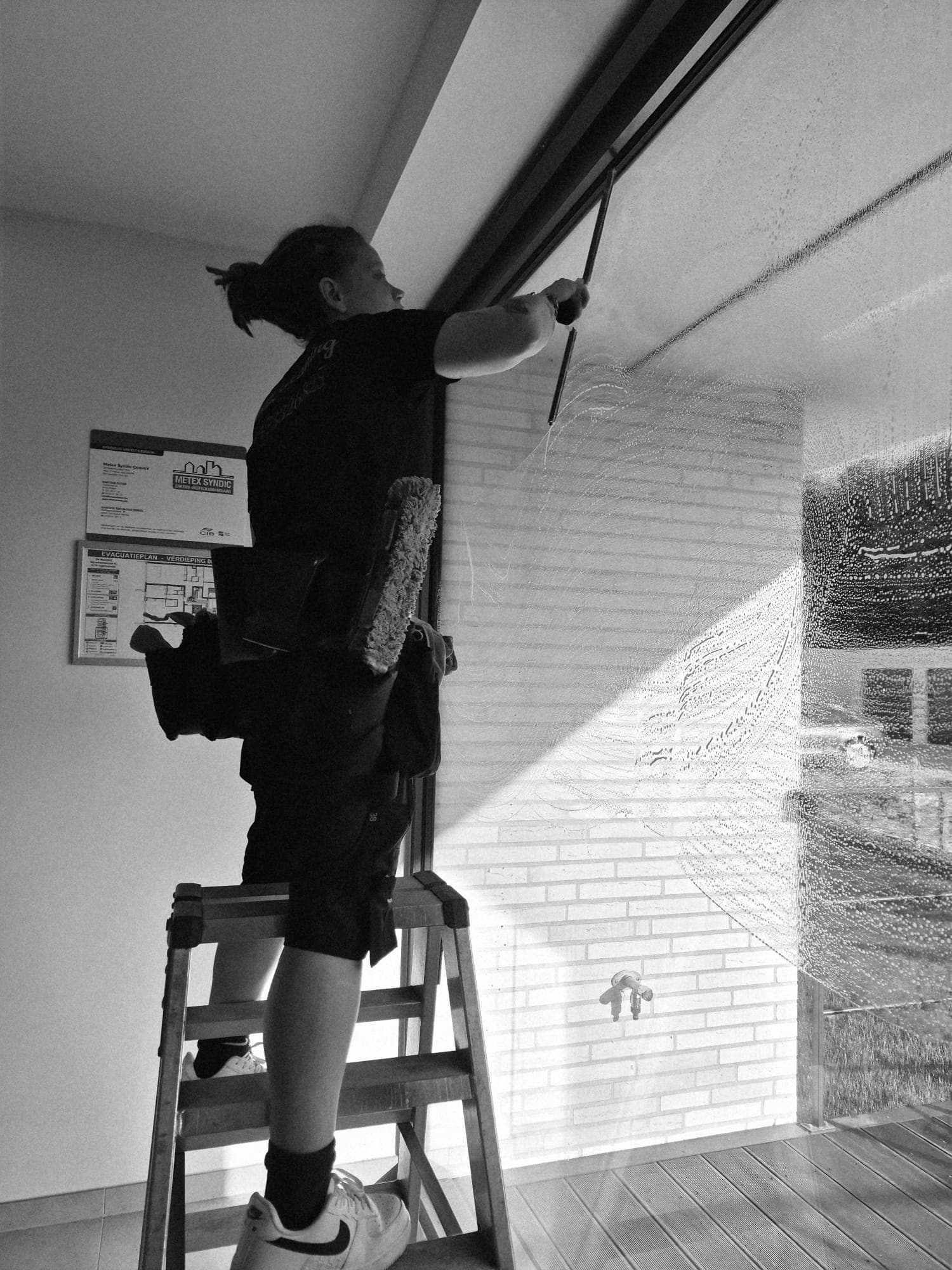 Glazenwasser op een ladder poetst een raam in een appartementsgebouw