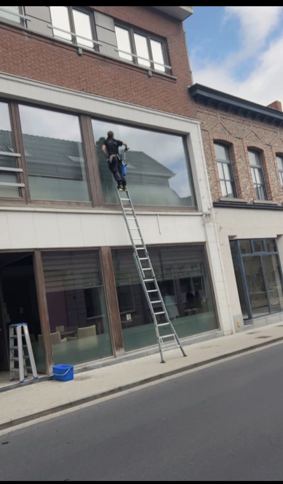 Glazenwasser op een hoge ladder poetst grote ramen aan een gevel