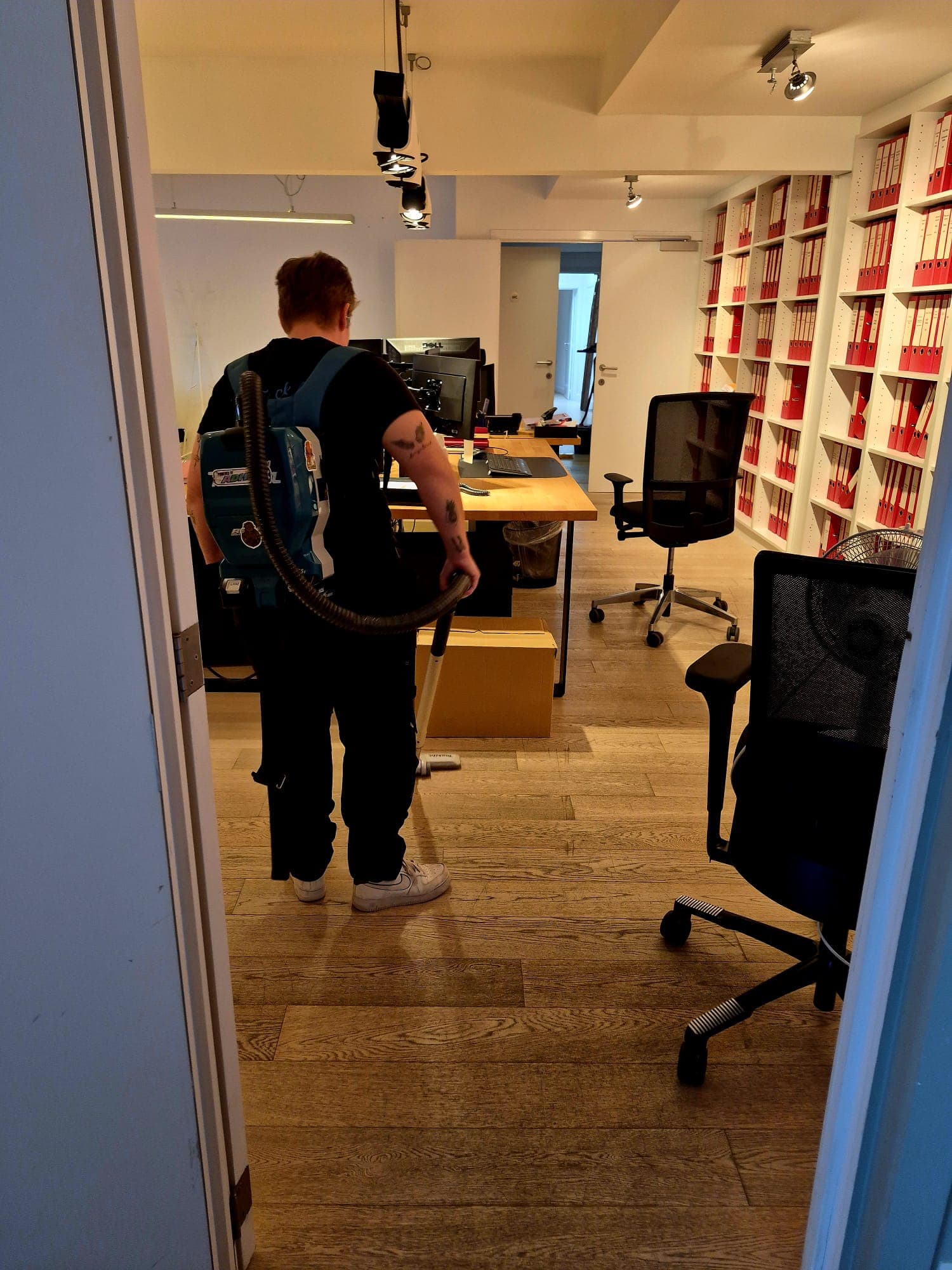 Medewerker van Shaz Cleaning stofzuigt een kantoorvloer met rugstofzuiger